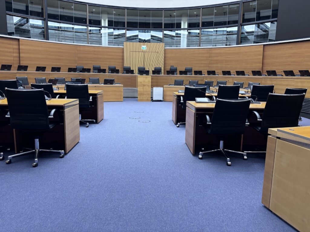 Court room, blue carpet; brown wooden desks and black chairs arranged in a semi circle