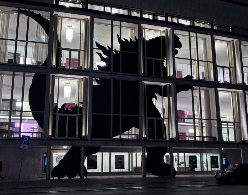 Silhouette of godzilla against illuminated windows